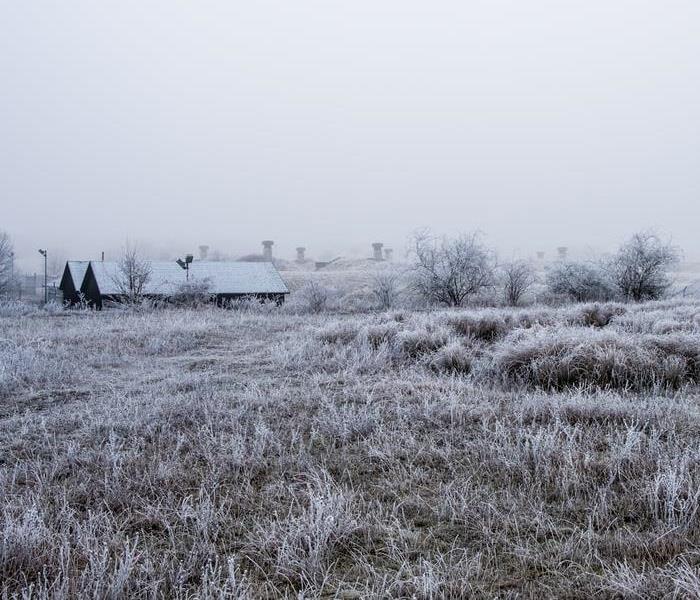 frozen plain with grass and a house, covered in snow.
